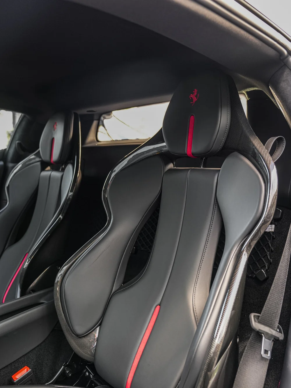 Dark Ferrari seats with red vertical accents and embroidered prancing horses