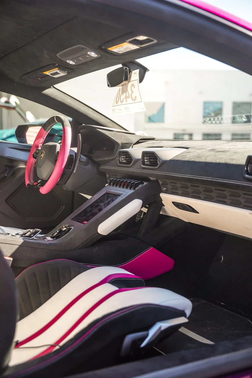 Pink Lamborghini cabin with the dashboard, steering wheel and white seat visible