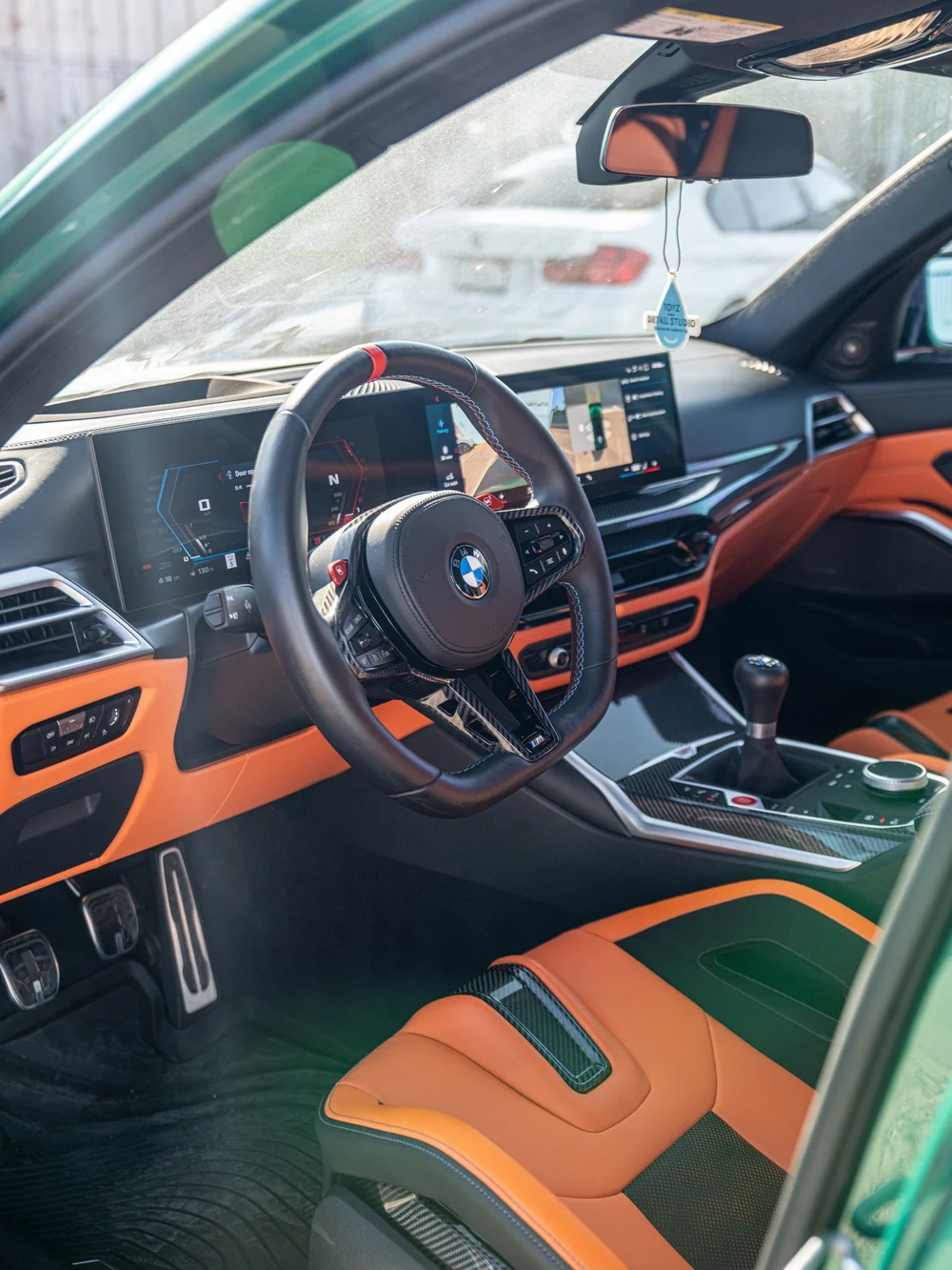 Driver cockpit of the manual G80 BMW M3 showing the shifter, steering wheel and Kyalami Orange interior