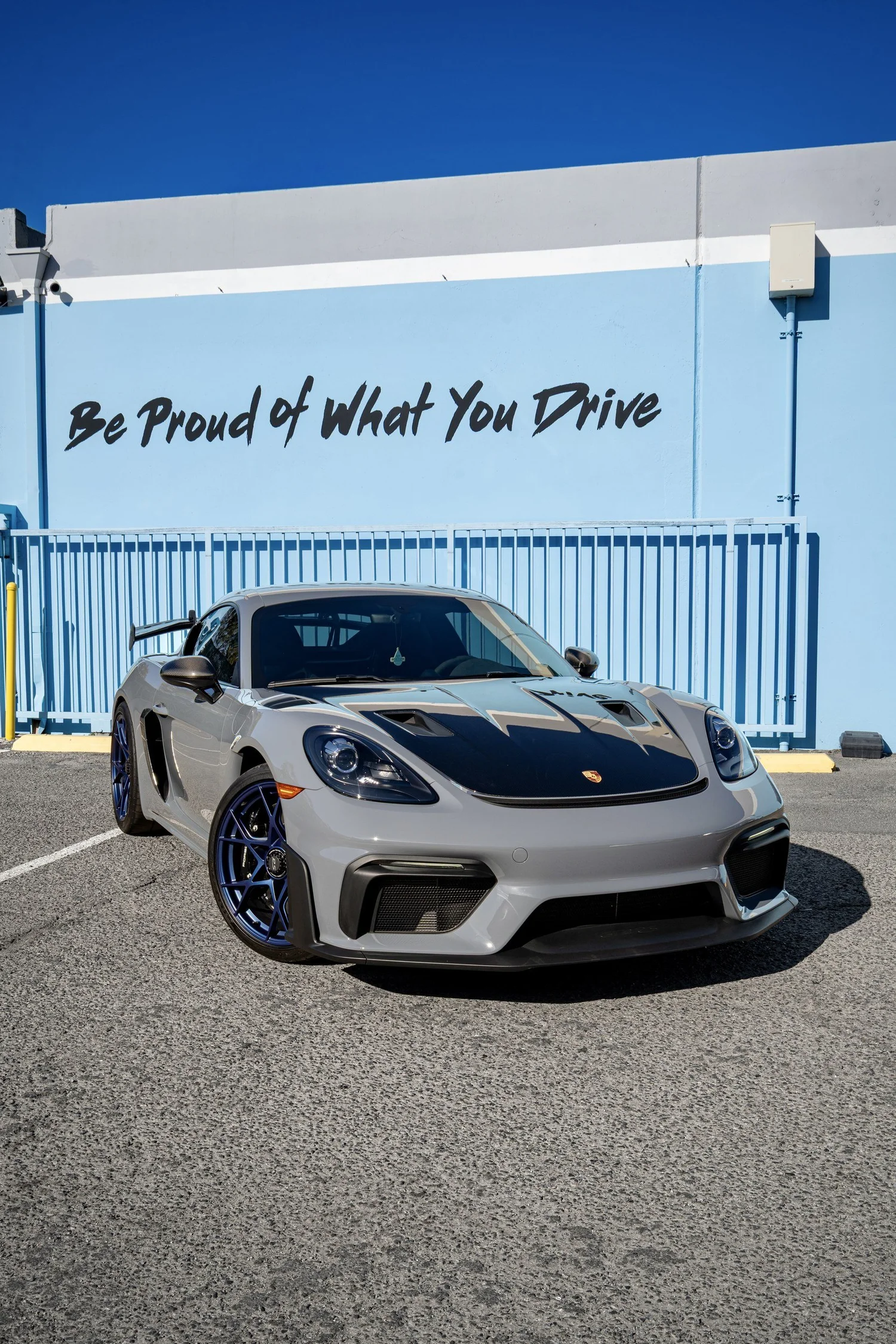 Front three-quarter view of the Arctic Grey 2025 Porsche 718 Cayman GT4 RS, with a carbon hood and blue wheels outside Toyz.