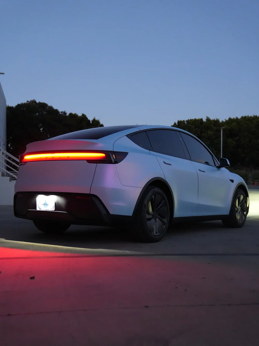 Low rear three-quarter view of a Tesla Model Y with a blue cast on its color-shifting vinyl