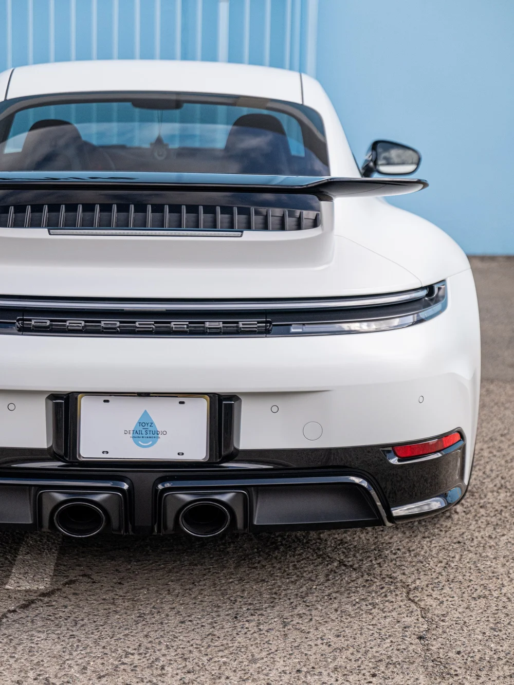 Rear bumper close-up of a Porsche 992.2 Carrera 4 GTS showing satin-white bodywork, the taillight strip and gloss-black lower trim