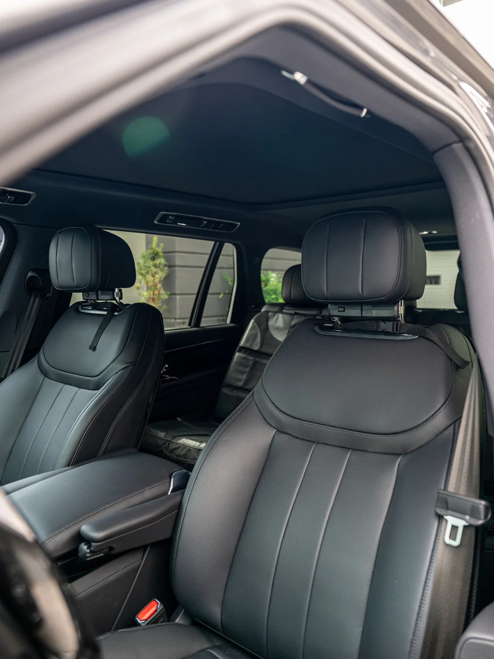 Range Rover front-seat and cabin view through the open door, showing the seat headrests and panoramic glass roof above.