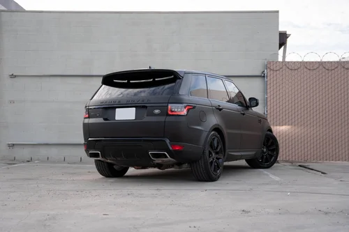 Rear three-quarter view of the matte black vinyl-wrapped Range Rover beside a light concrete wall.