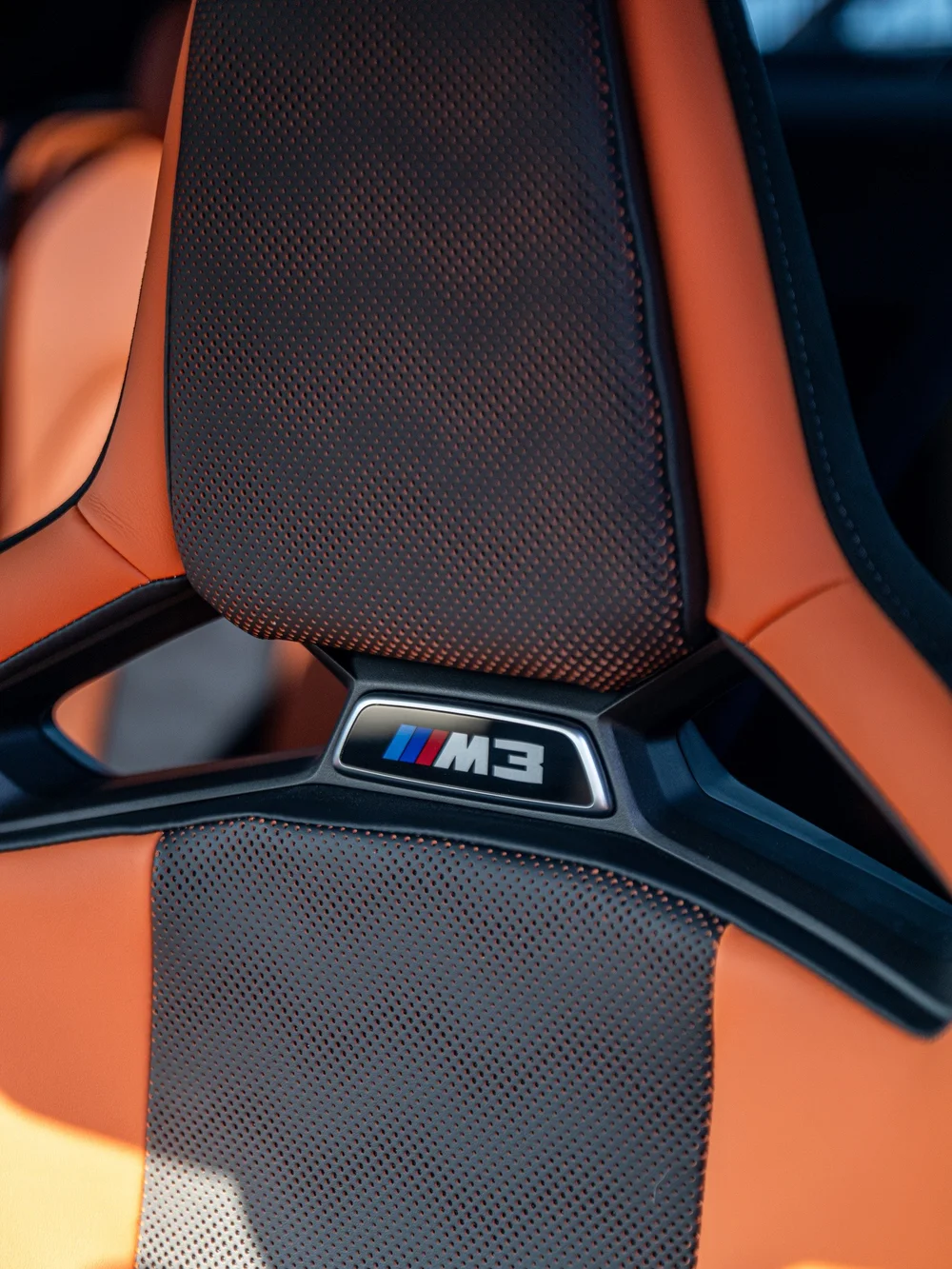 M3 badge and orange leather surrounding the black seat backrest