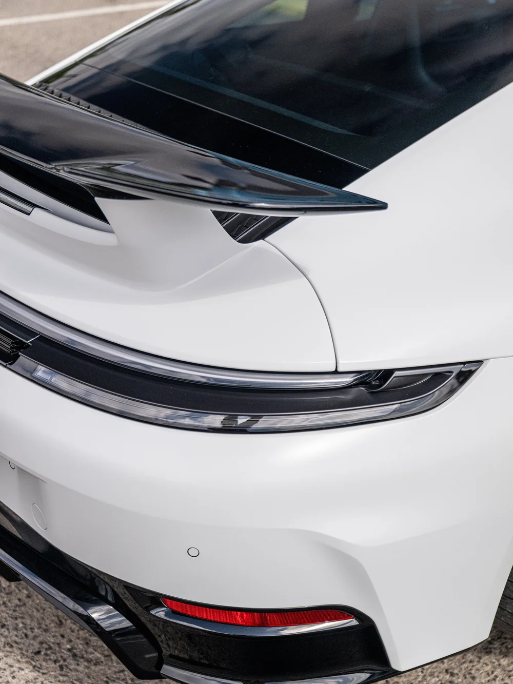 Gloss-black rear wing and taillight detail on a 2026 Porsche 911 Carrera 4 GTS with satin-white bodywork