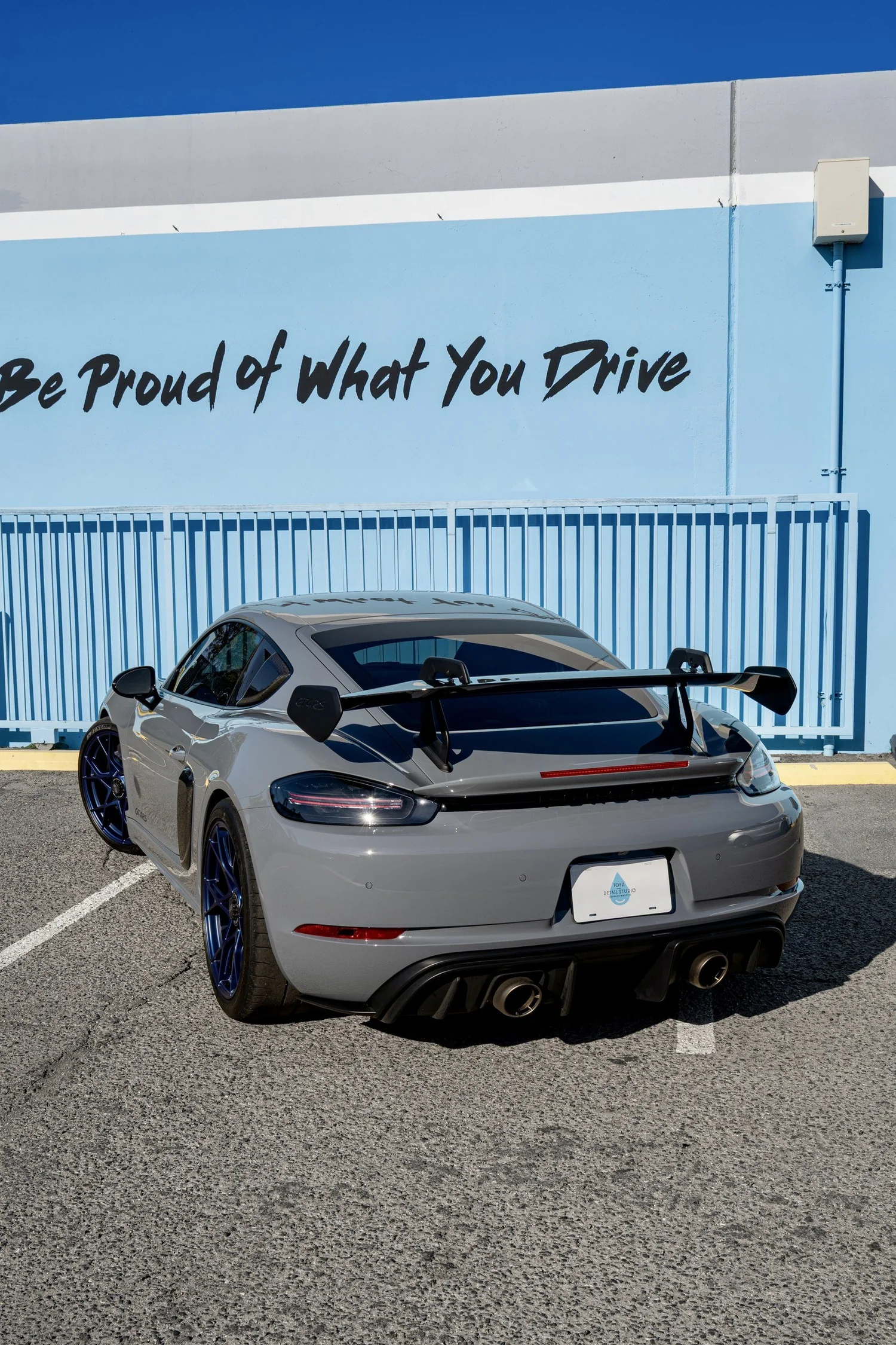 Rear three-quarter view of the Arctic Grey GT4 RS with its exposed-carbon rear wing, blue wheels and rear diffuser.