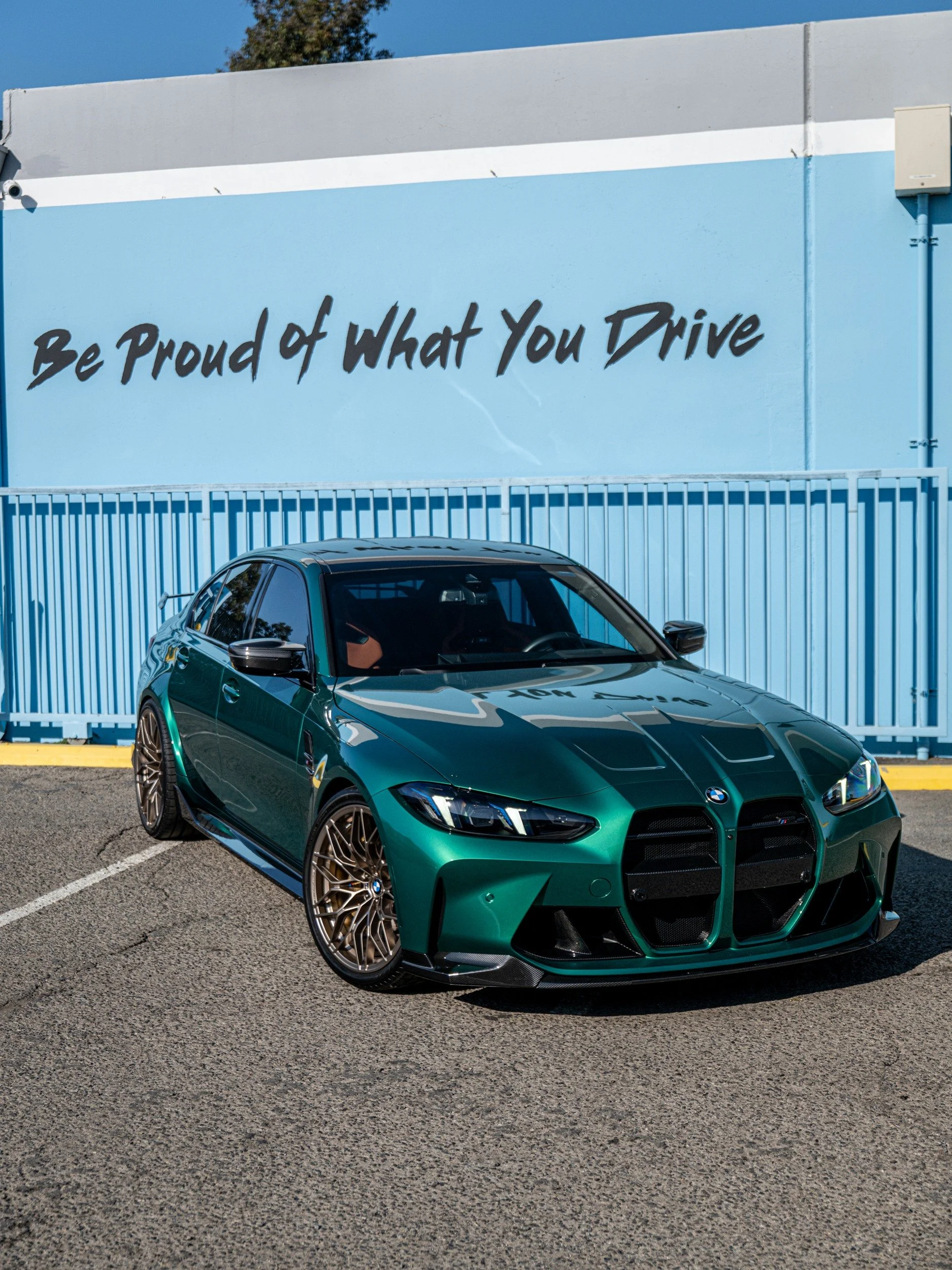 Front three-quarter view of the Isle of Man Green 2025 BMW M3 Sedan with bronze-toned wheels and exterior M Performance carbon