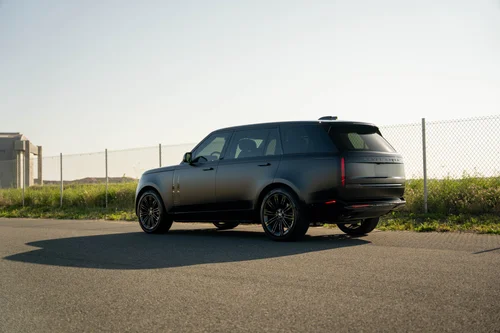 Rear three-quarter view of the black Range Rover with STEK DYNOmatte PPF beside a sunlit fence.