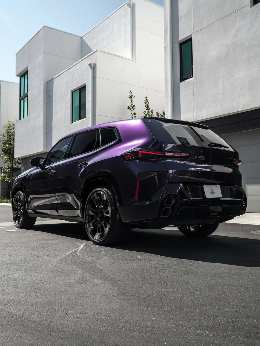 Low rear three-quarter view of the BMW XM with Venetian Mauve colored PPF in daylight