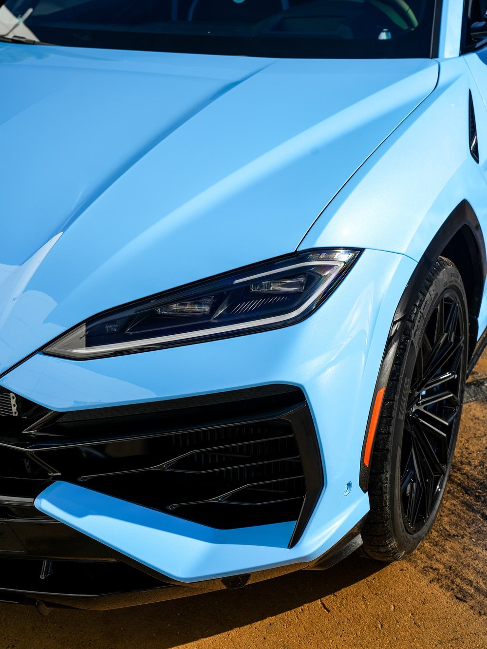 Light-blue Urus SE hood, headlight, front fender and black wheel in a close front-corner view