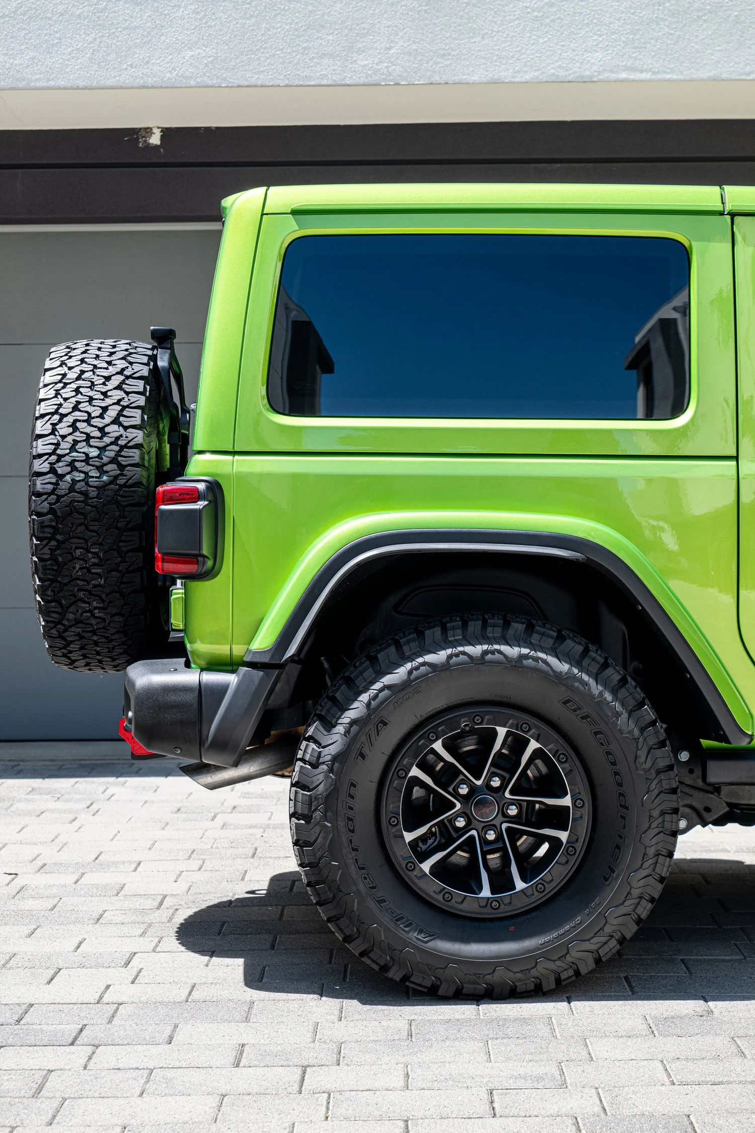 Rear wheel and Mojito quarter panel of the Rubicon beneath dark side glass, with the spare tire visible at the rear