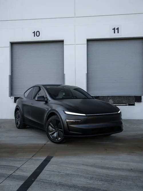Tesla Model Y with 3M Satin Black vinyl, front three-quarter whole-car view outside the studio