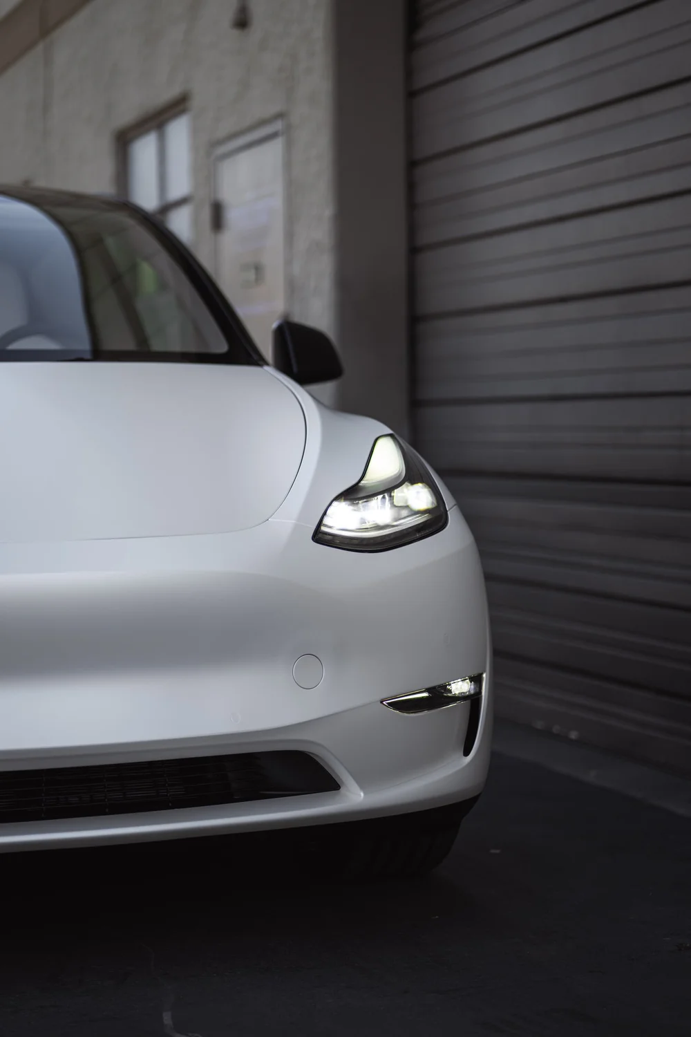 Closer front-corner view of the Satin Pearl White Tesla Model Y showing its illuminated headlight
