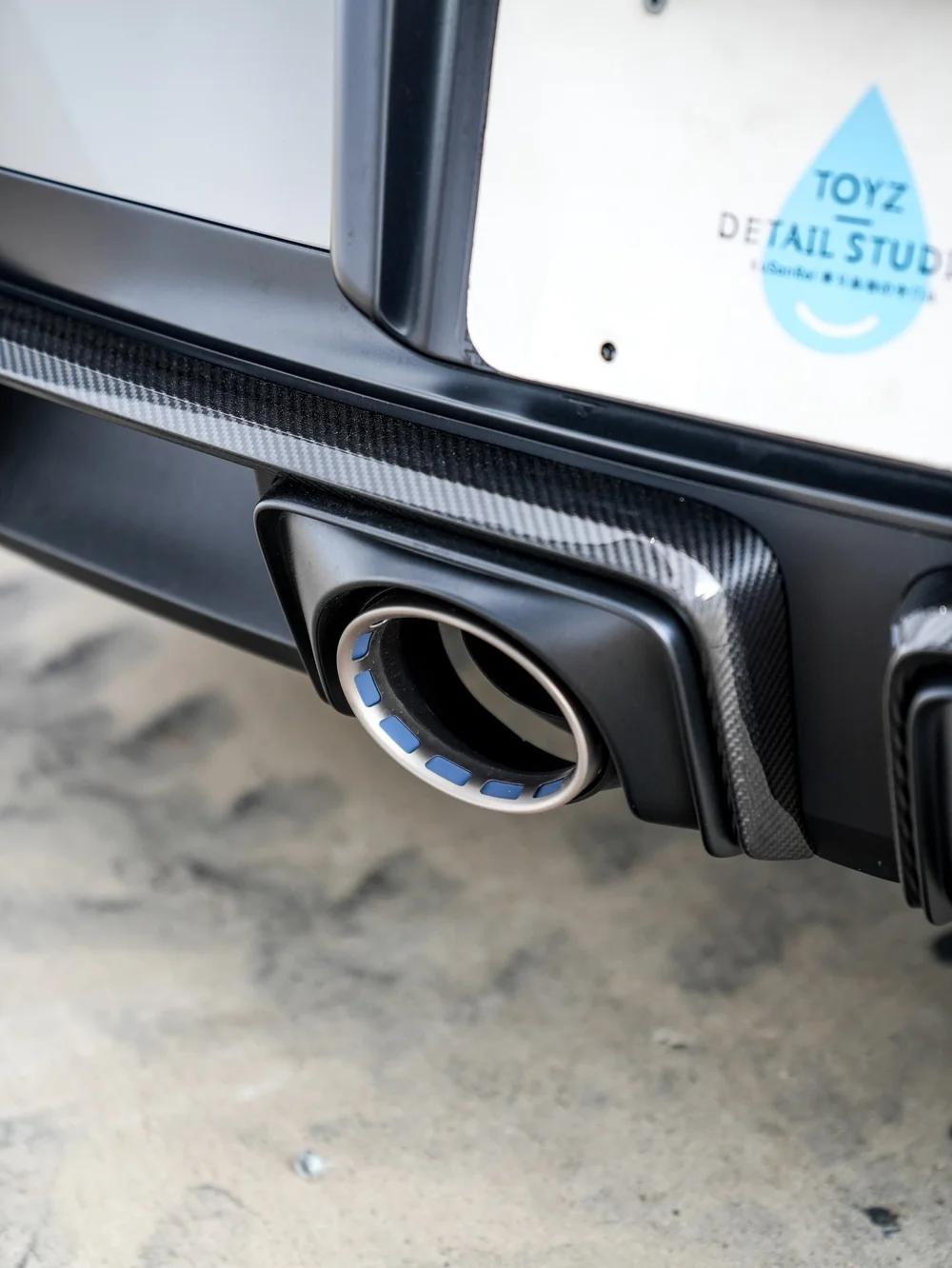 Round Porsche exhaust outlet beneath the Toyz plate and dark patterned rear trim