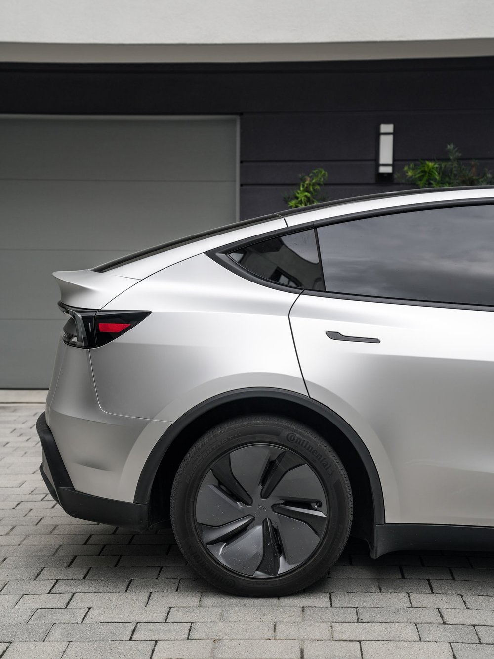 Tesla Model Y rear wheel cover beneath matte-silver quarter panels and dark side glass