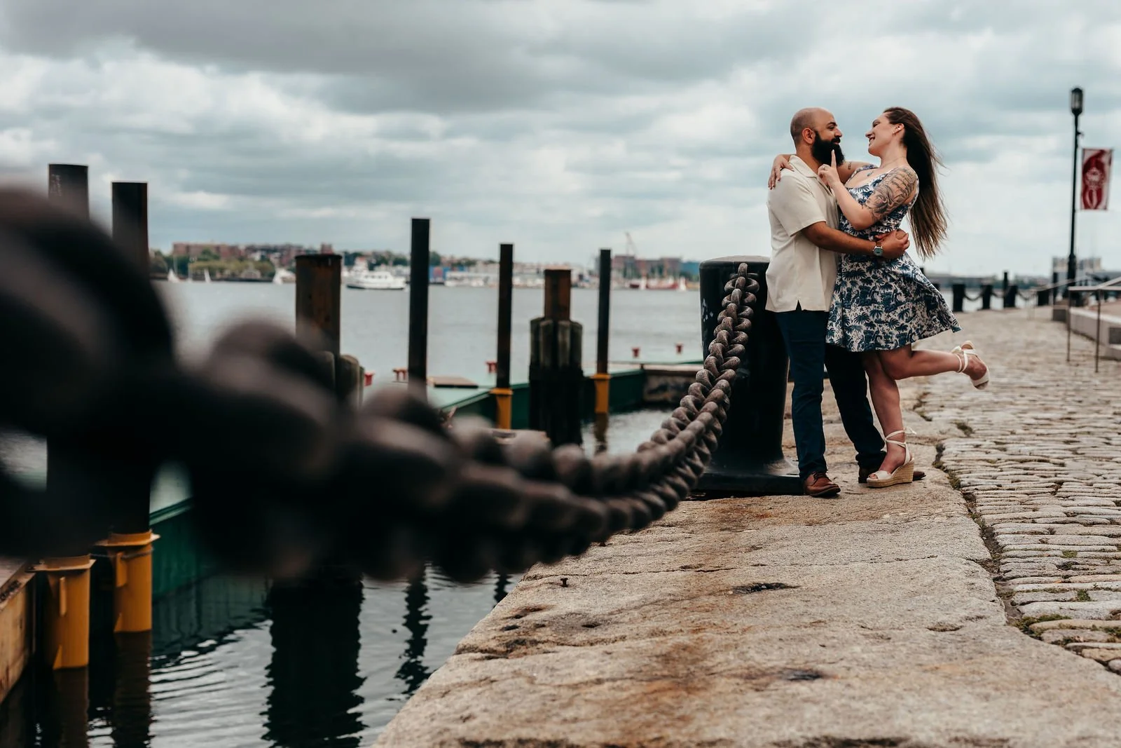 Wide engagement photo of the couple on a pier under dramatic skies in Seaport Boston