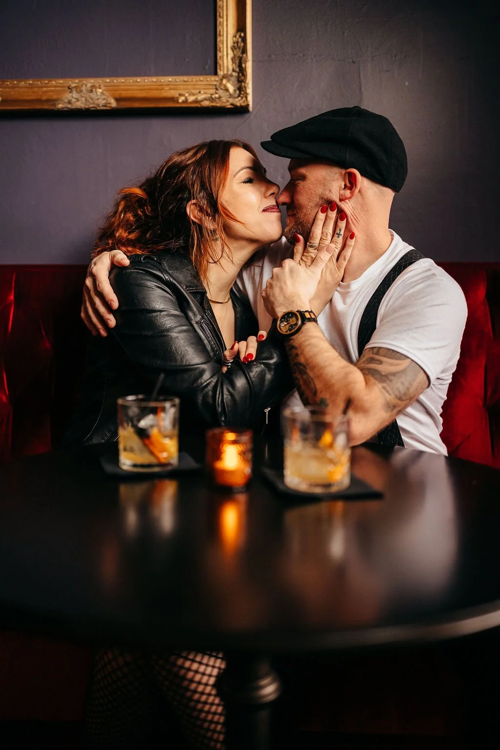 Kristin and Mike kissing at a candlelit table in a red velvet booth, Laconia engagement photographer