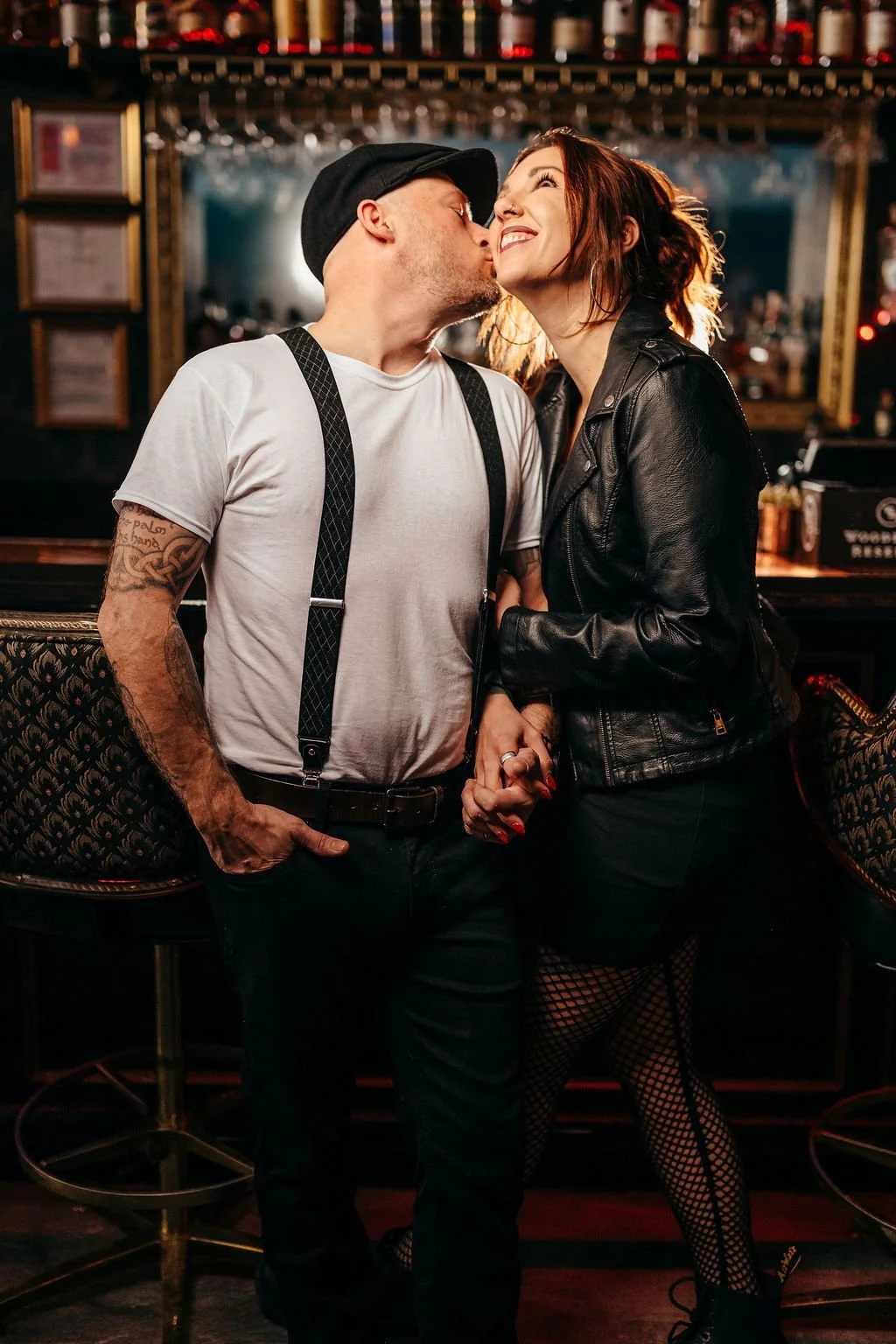 Mike kissing Kristin's cheek while holding hands at the bar, speakeasy engagement photos