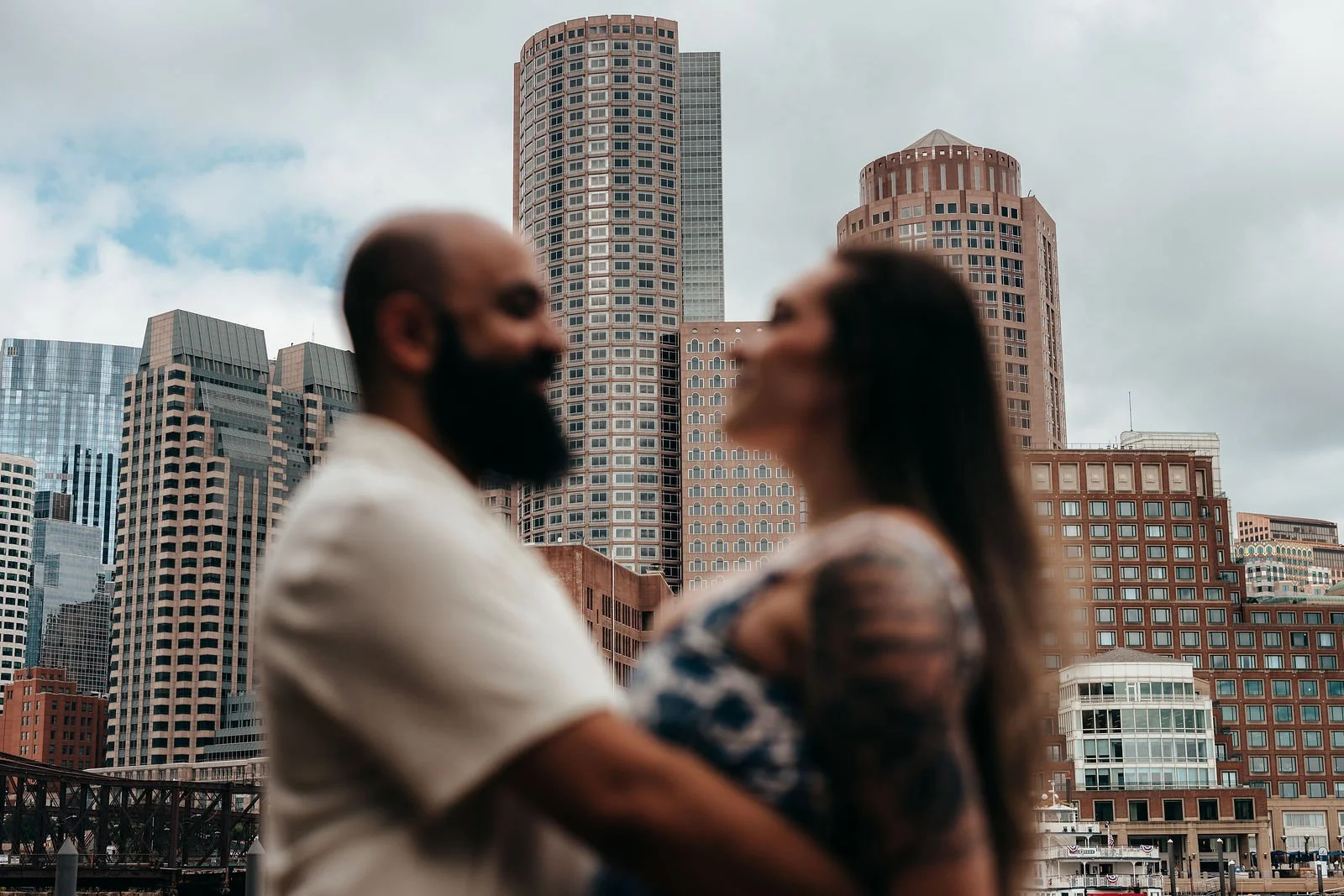 Aziz and Katherine embracing with the Boston skyline behind them