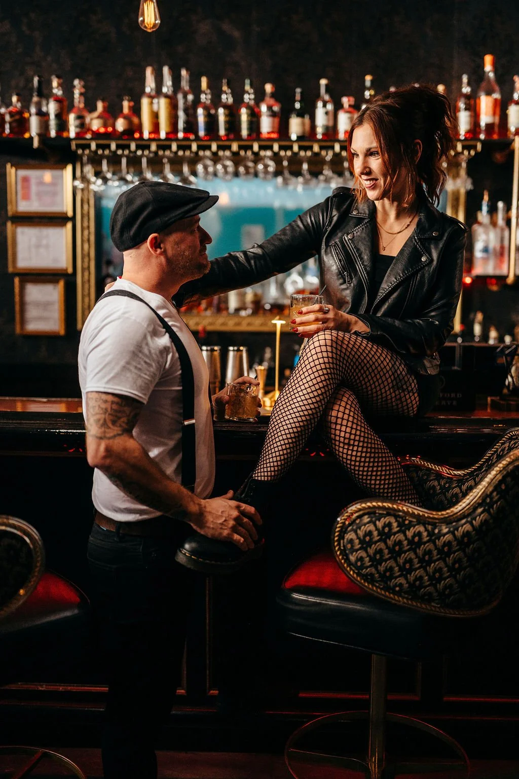 Kristin sitting on the bar in fishnets and leather jacket during their speakeasy engagement photos
