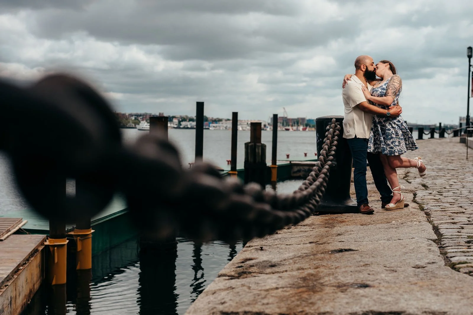 Aziz kissing Katherine on a pier framed by chains, Boston engagement session