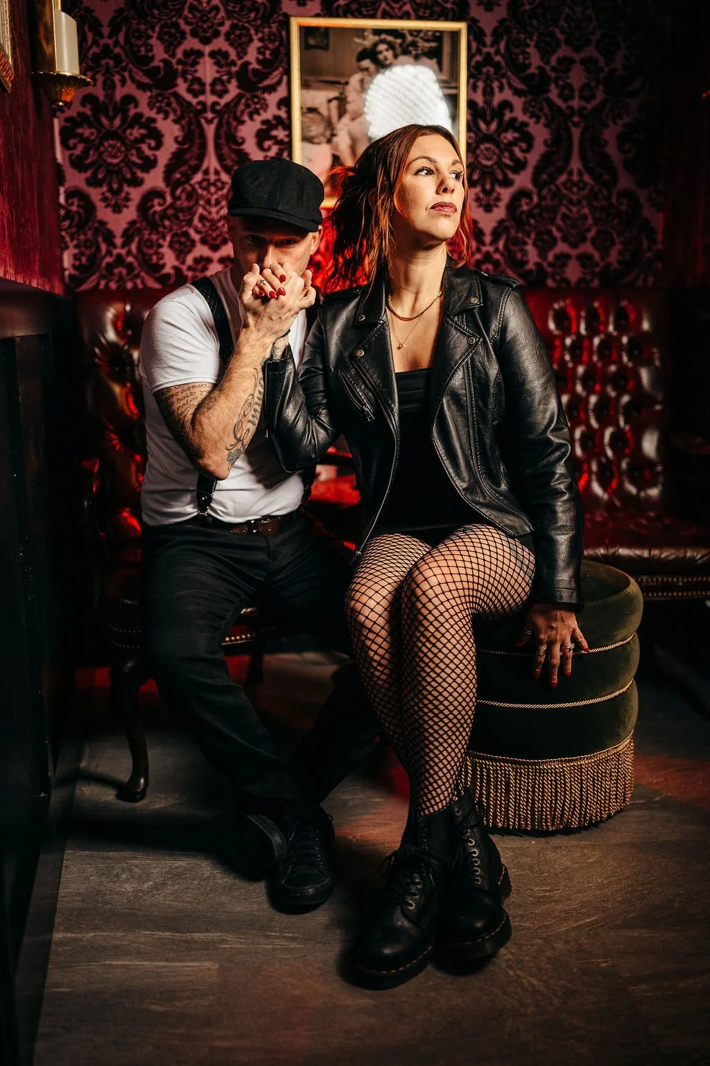 Stylish moody portrait of Kristin and Mike on leather furniture with red damask wallpaper