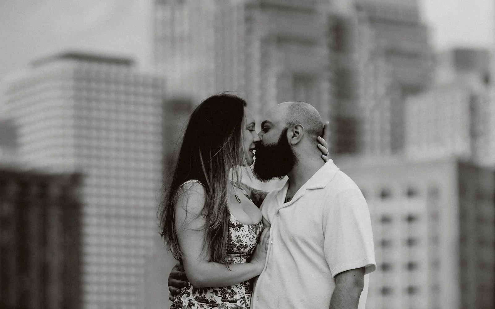 Black and white photo of the couple kissing with the Boston skyline
