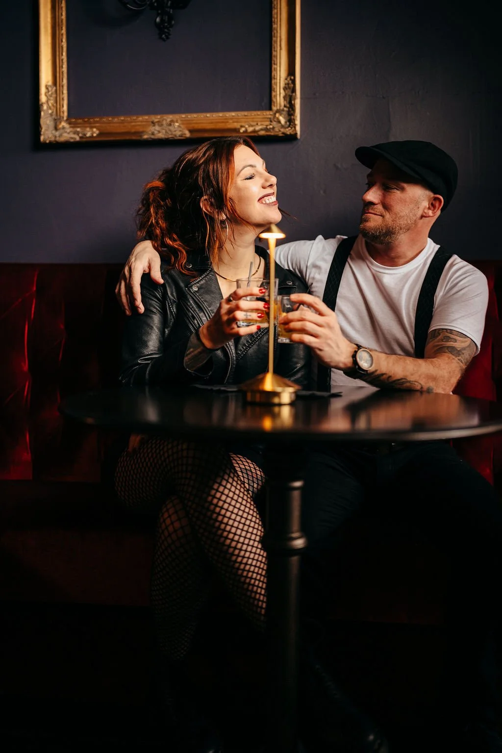 Kristin laughing with Mike over drinks in a red velvet booth at The Candy Bar