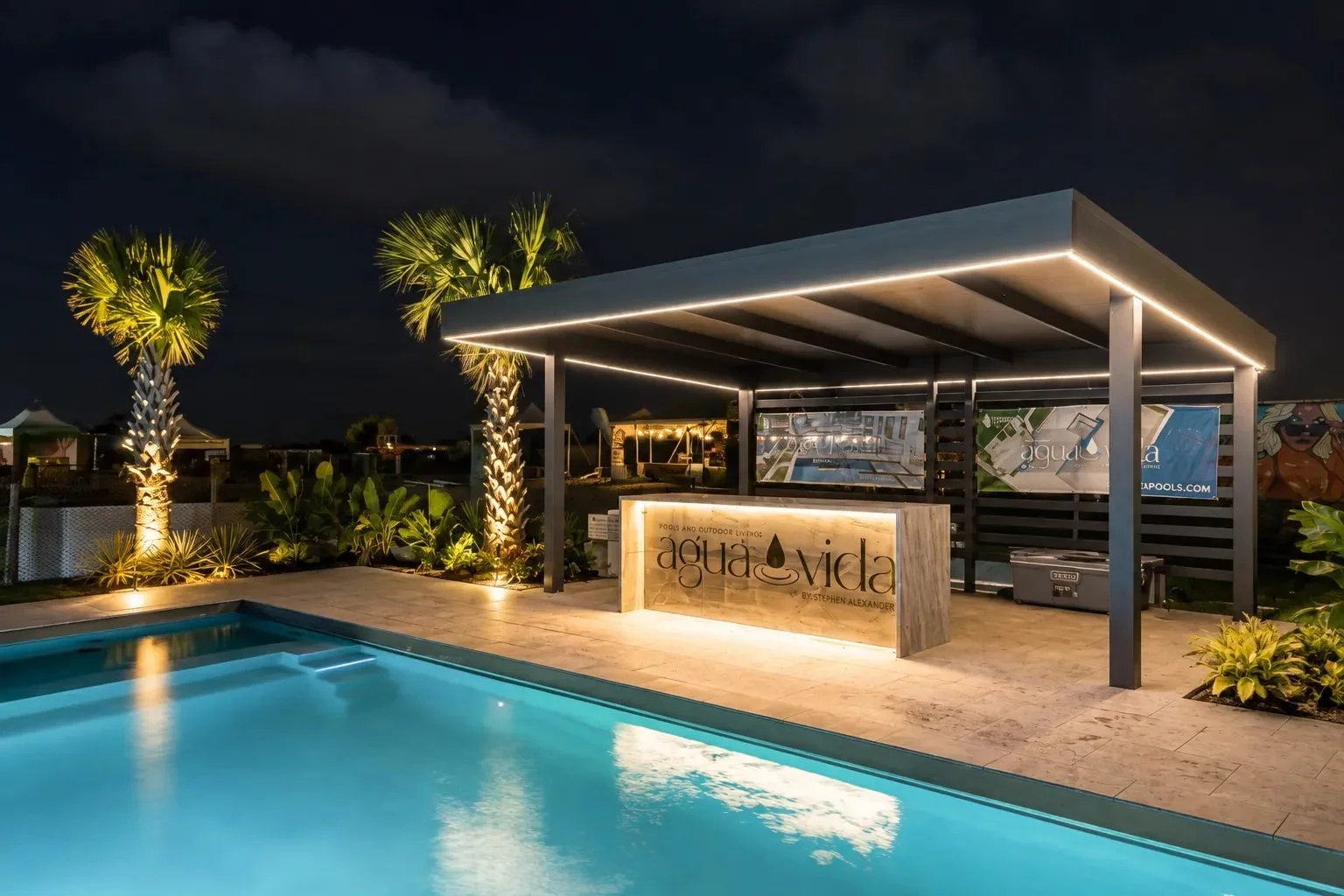 Louvered pergola with lighting over a poolside lounge at dusk