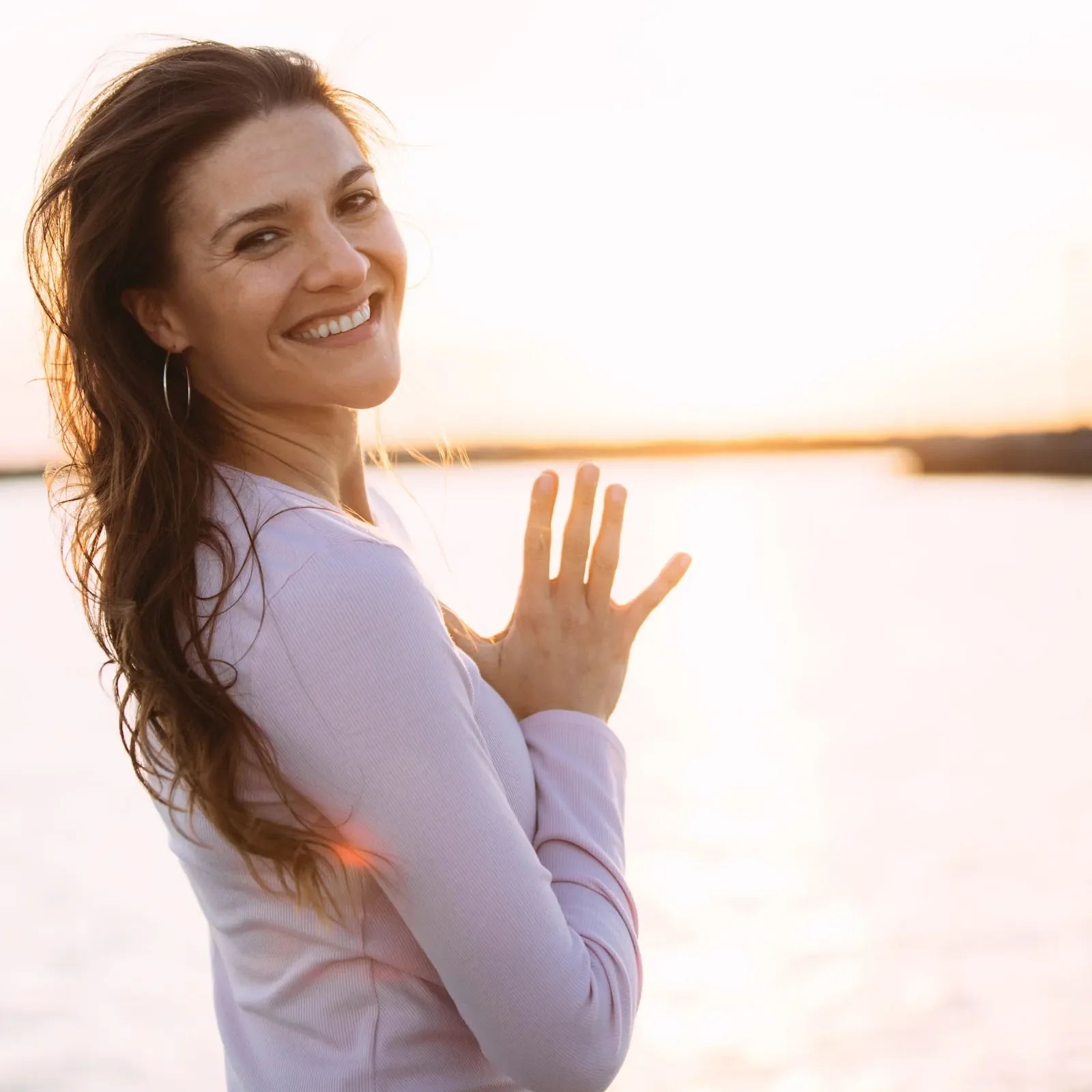 Josie Kramer smiles and waves by the water in warm sunset light