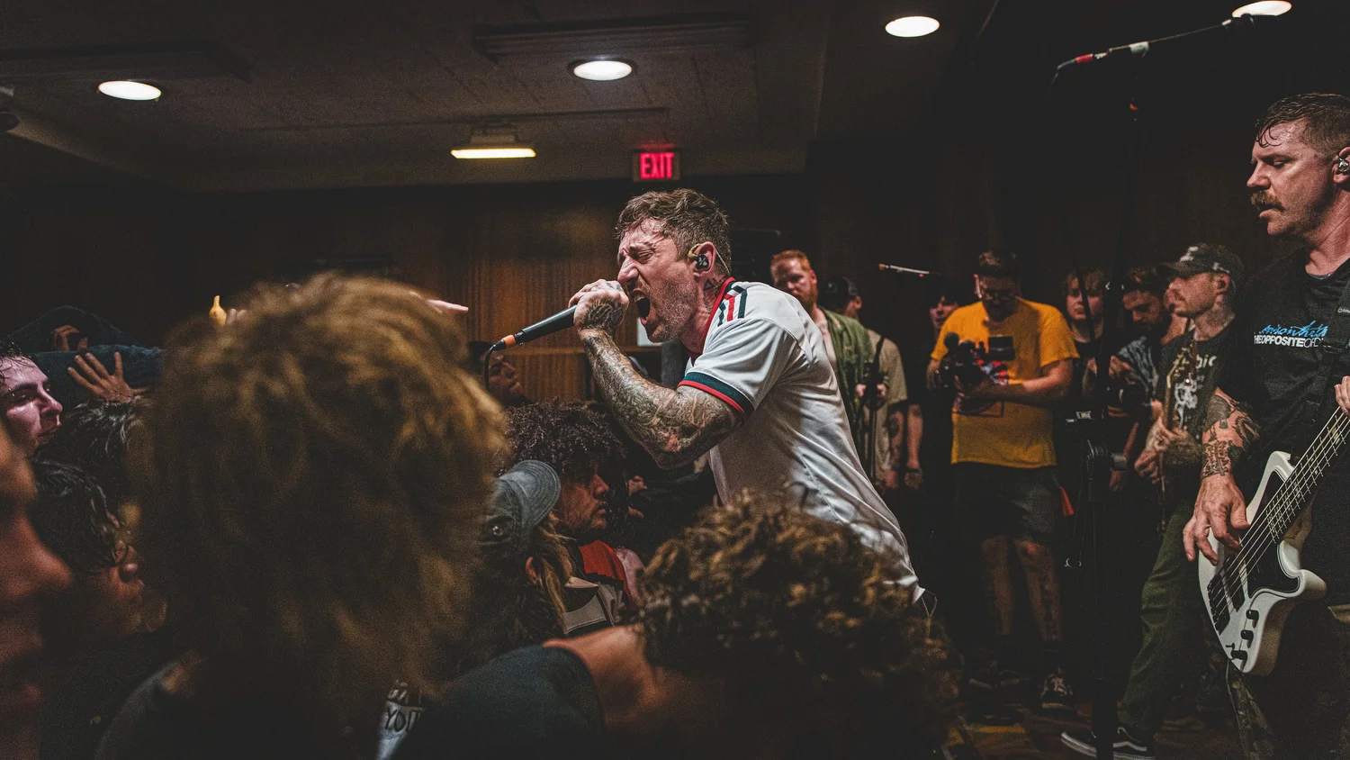 VANNA vocalist singing into a handheld microphone beside the bassist as the crowd presses toward the stage