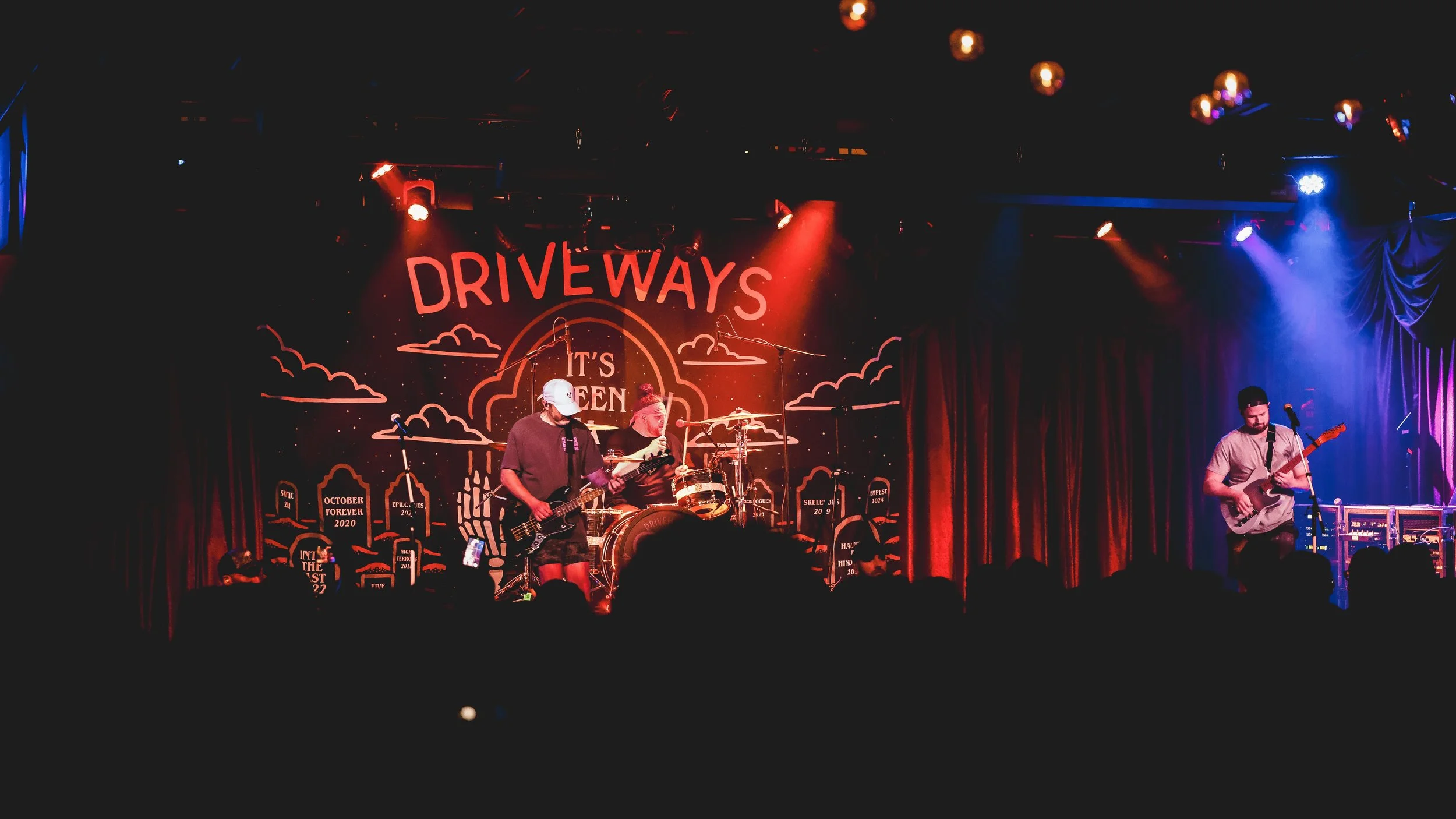 Driveways guitarist leaning into a performance under vivid blue and magenta concert lighting