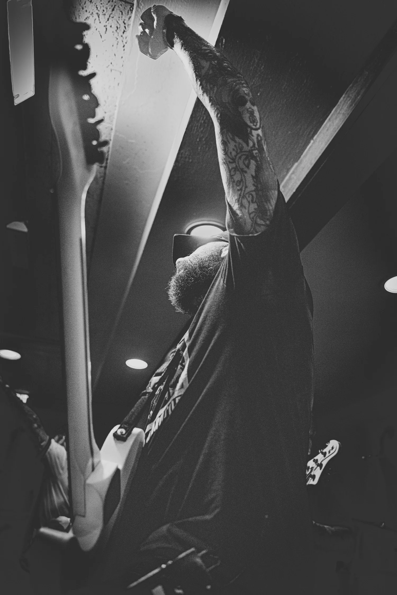 Black-and-white low-angle view of a tattooed VANNA guitarist raising one arm while holding a guitar