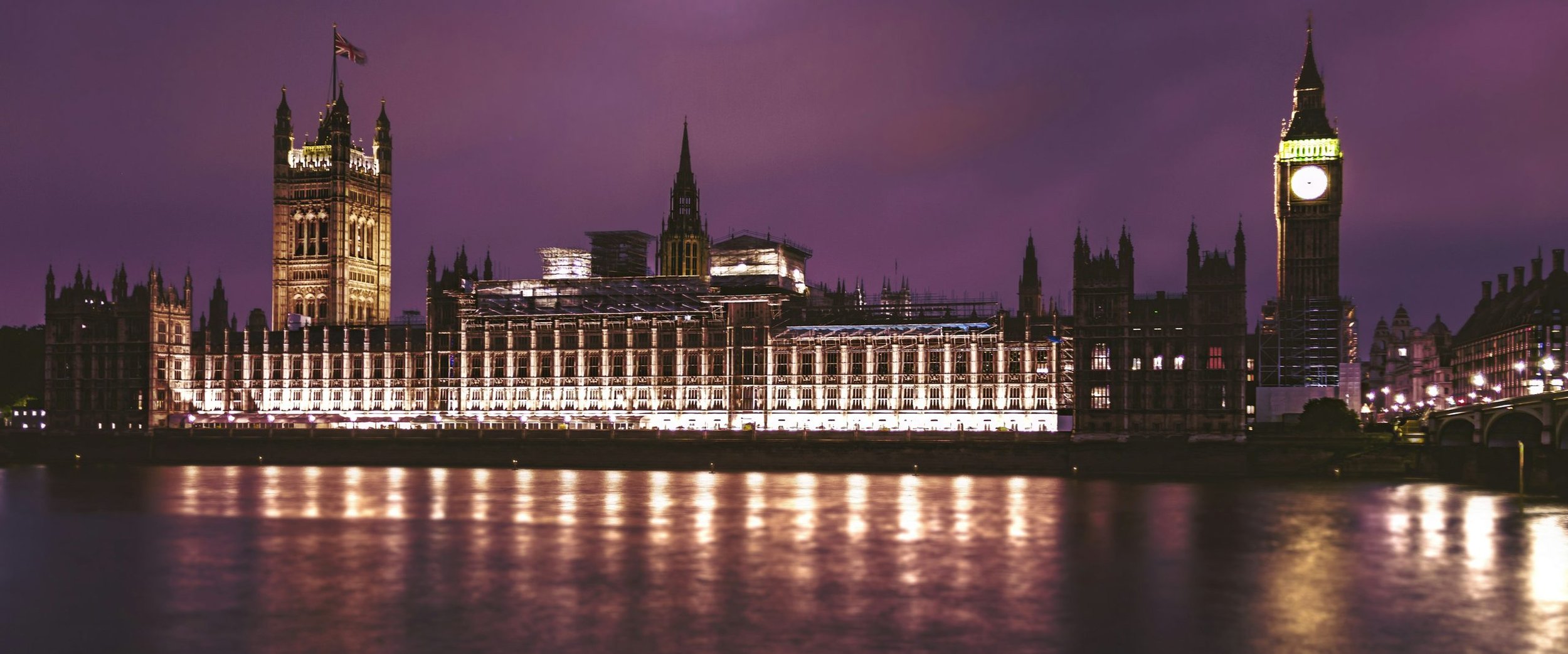 The Palace of Westminster lit across the River Thames under a violet dusk sky