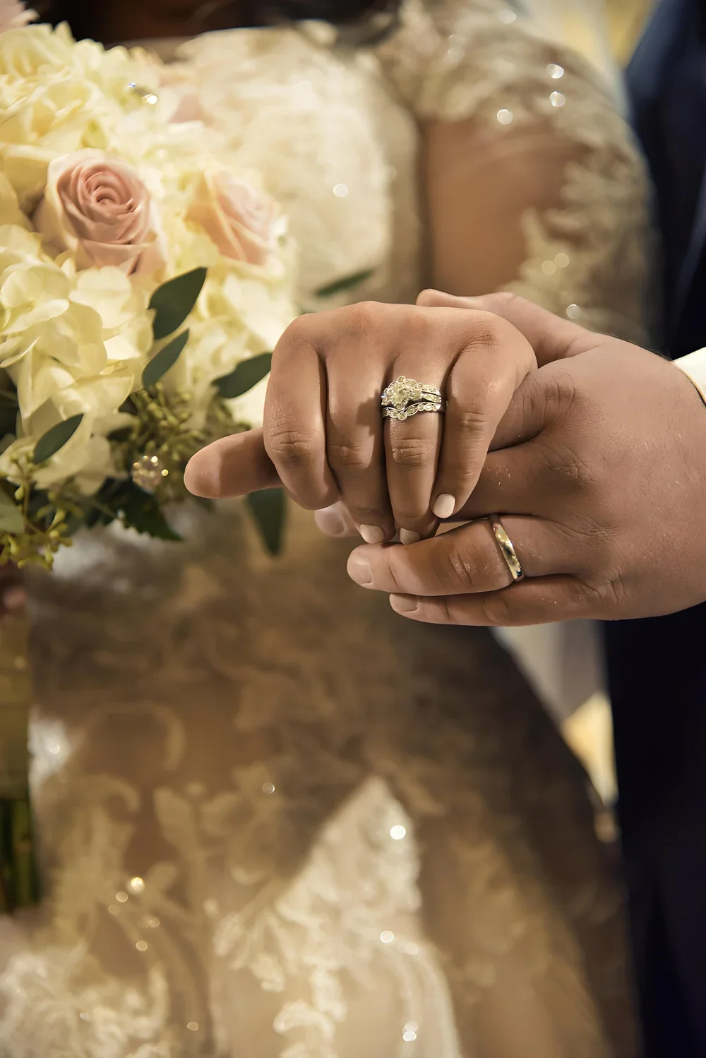 A newlywed couple’s hands showing their wedding rings beside a bridal bouquet