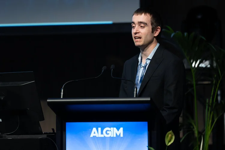 Head and shoulders photo of Callum McMenamin. He has short brown hair, a beard, and is wearing a grey T-shirt, and is looking at the camera.