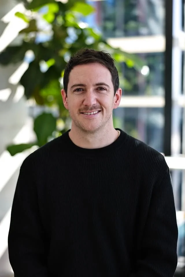 Head and shoulders photo of Callum McMenamin. He has short brown hair, a beard, and is wearing a grey T-shirt, and is looking at the camera.