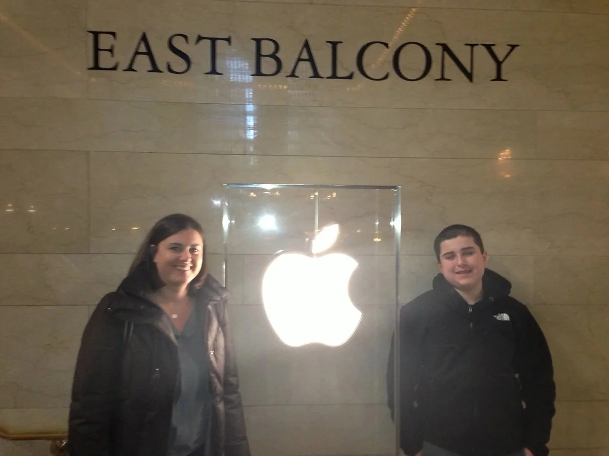 Michele and Matt beneath the Apple logo at Grand Central Terminal