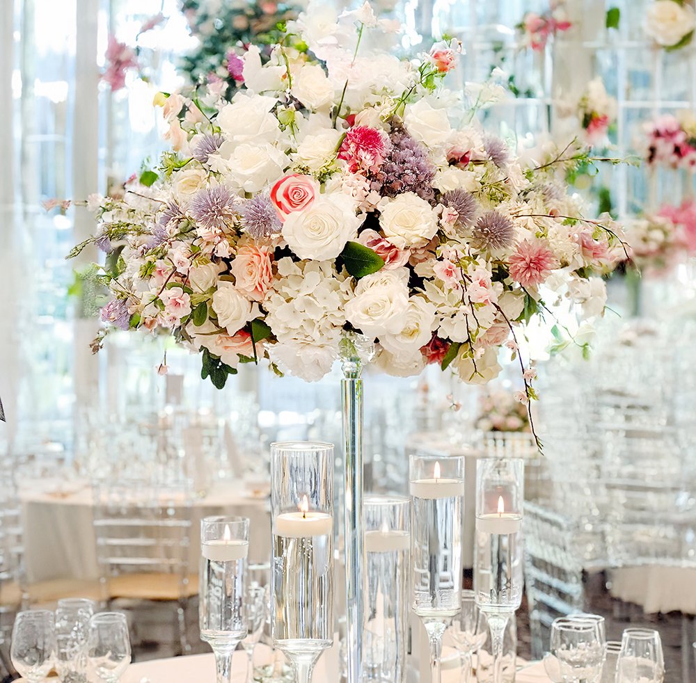 Elegant pink and white wedding centerpiece with tall floral arrangement, floating candles and clear chairs at The Guild Inn.