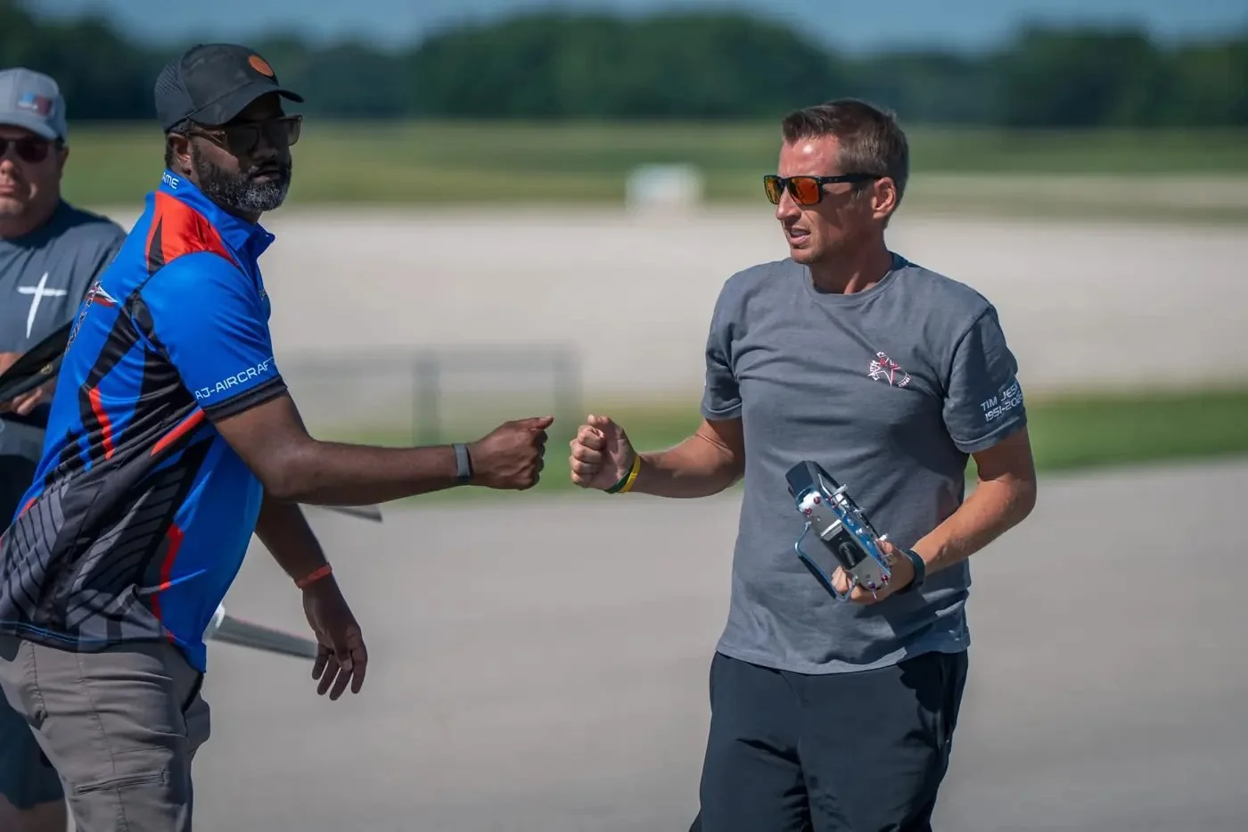 A Team USA pilot wearing a shirt with TIM JESKY 1951–2026 on the sleeve shares a fist bump with AC Glenn on the flightline.