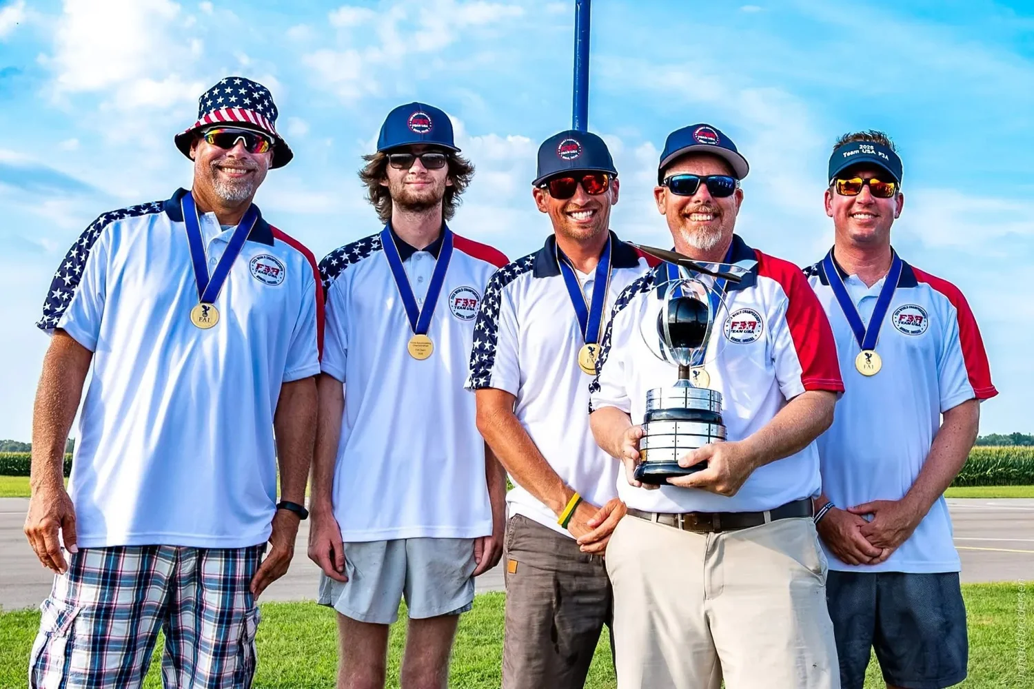 Team USA in stars-and-stripes polos and FAI gold medals, holding the World Championship team trophy on the flightline in Muncie, Indiana.