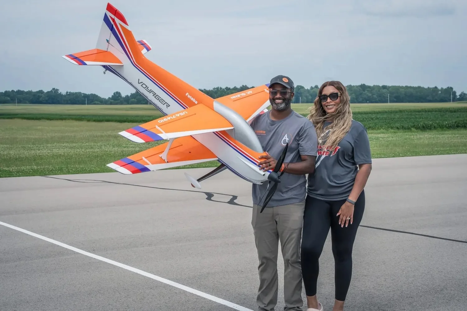 AC Glenn and his wife, Jasmine Glenn, on the runway with his orange Voyager F3A aircraft.