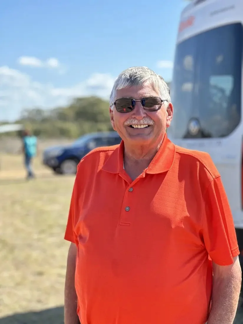 Tim Jesky, smiling in sunglasses and an orange polo, at a flying field.