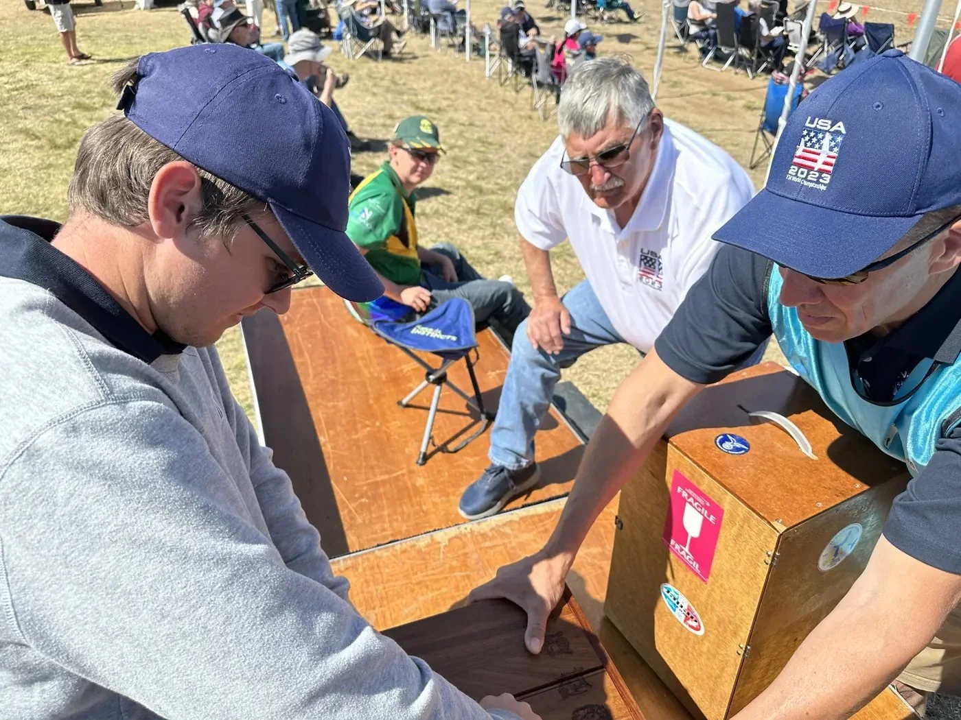 Tim Jesky, in a white USA polo, watching as team members handle equipment cases on the flightline.