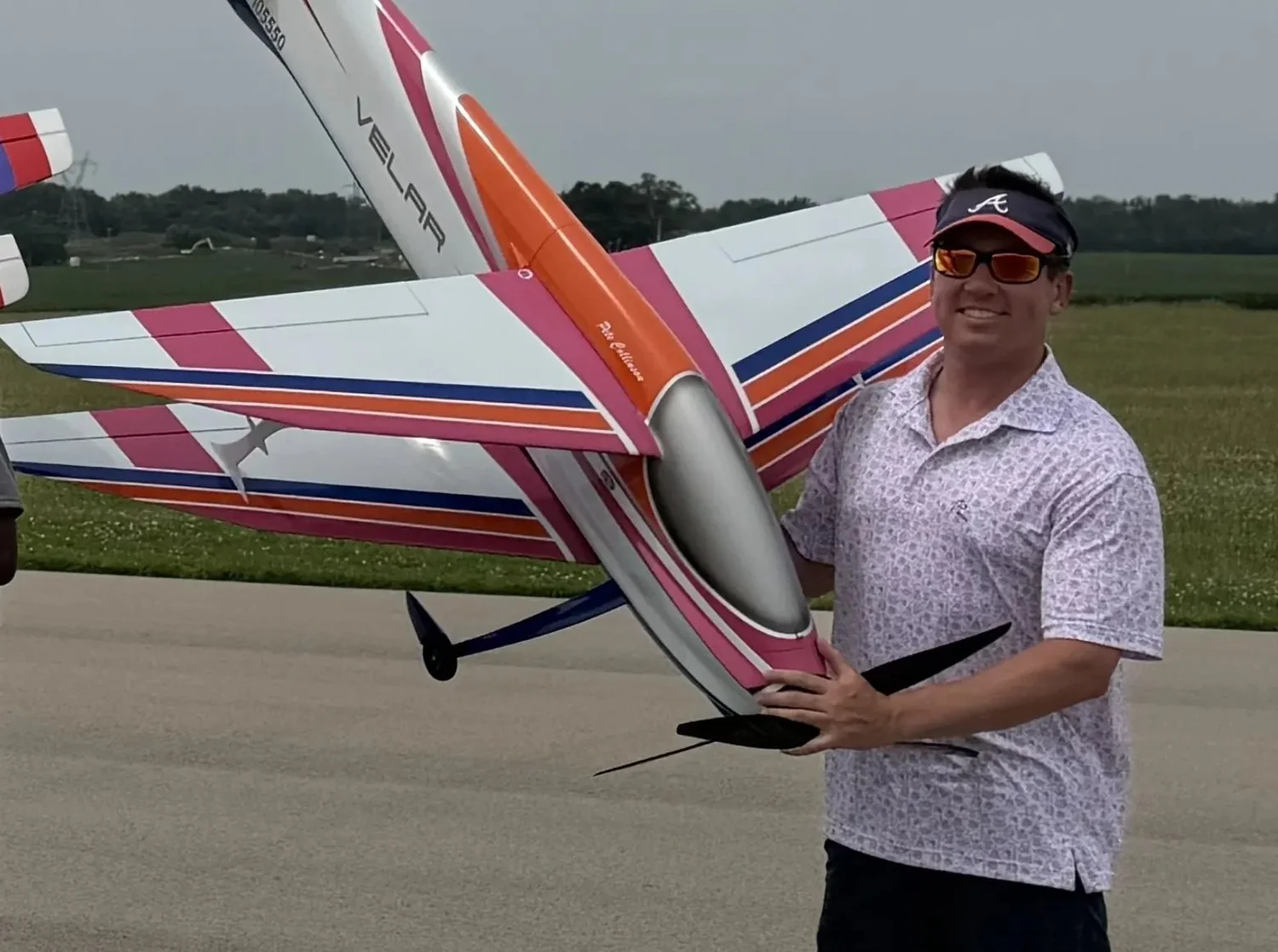 A Hui Yang Velar F3A biplane in pink, orange and white, held on the runway by Team USA alternate Pete Collinson.