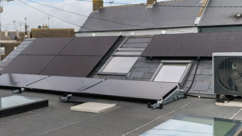 Solar panels installed on a slate roof and flat roof in an Irish town, with a heat pump unit alongside