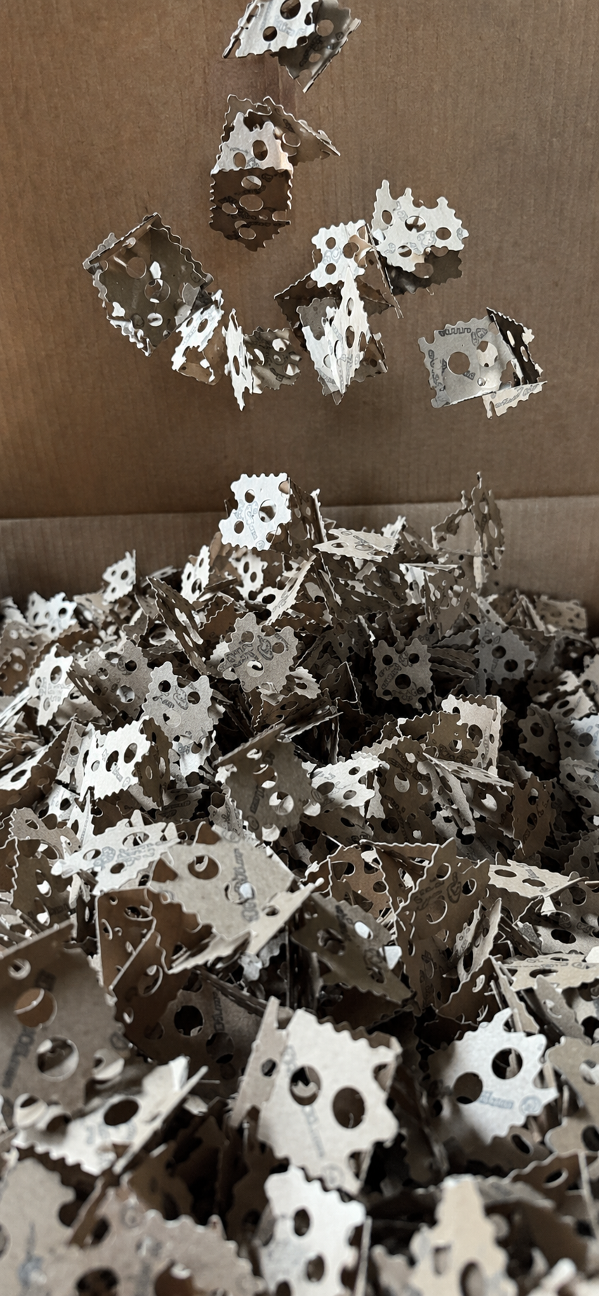 ExpandOS paper-based packing pieces pouring into a shipping box, interlocking cardboard triangles