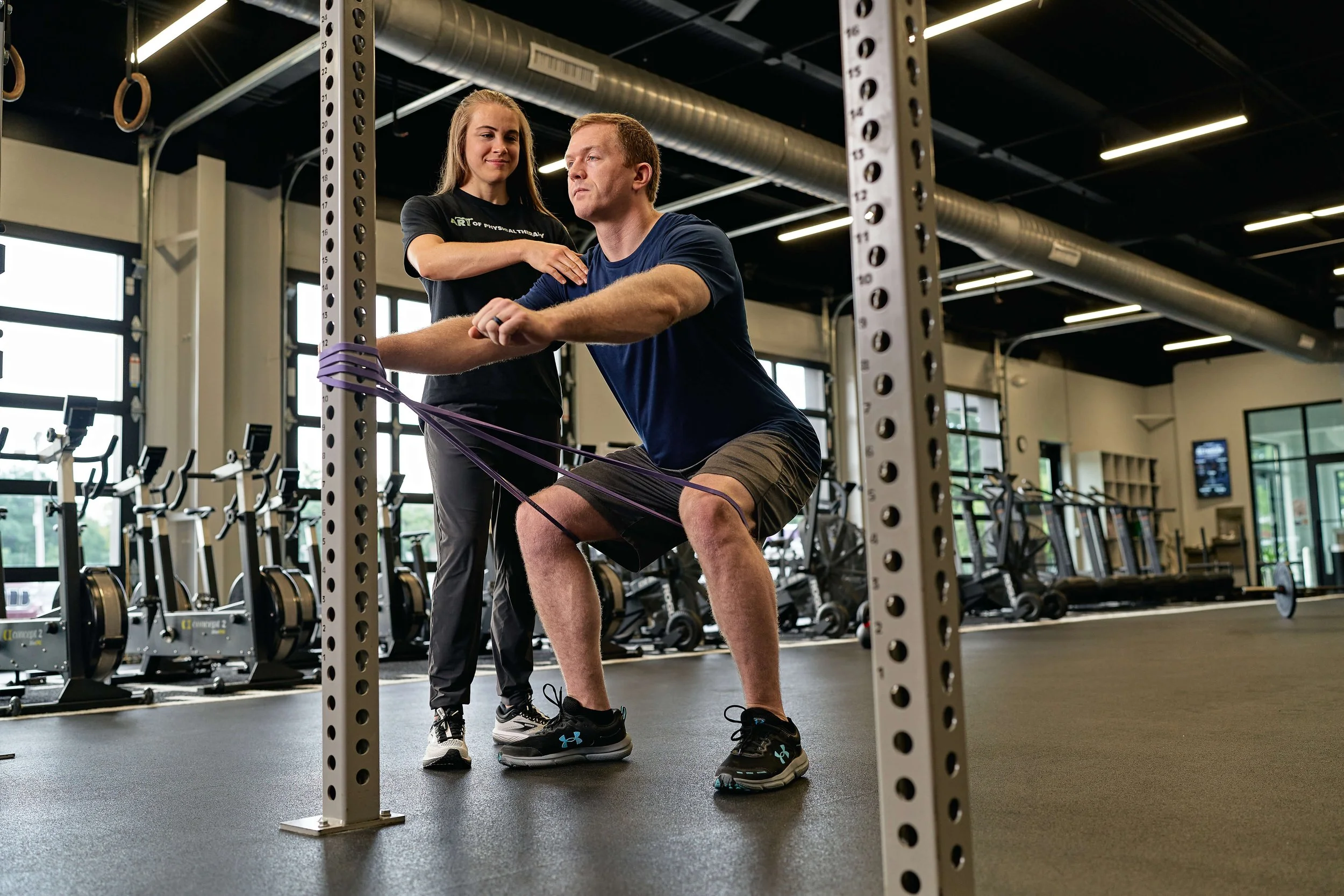 Physical therapist assessing an athlete performing a banded squat in Raleigh, NC