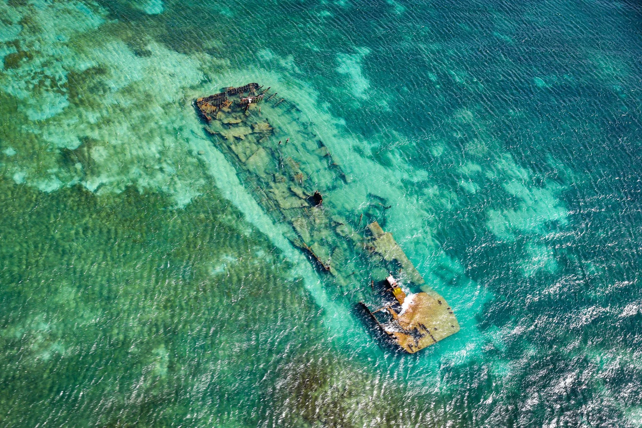 Turquoise water surrounding a long rock formation, photographed from above.